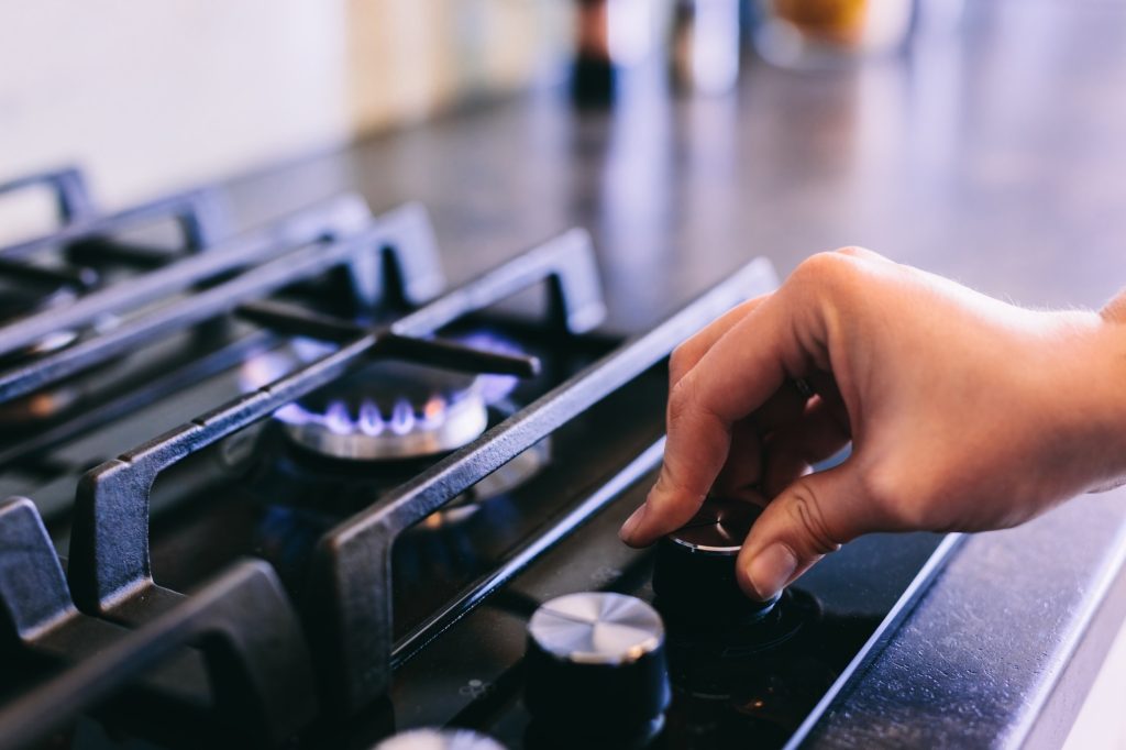 Hand turning on gas burner on kitchen stove top