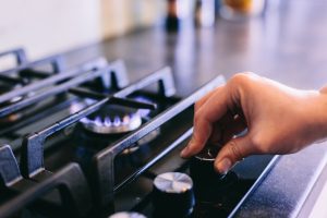 Hand turning on gas burner on kitchen stove top